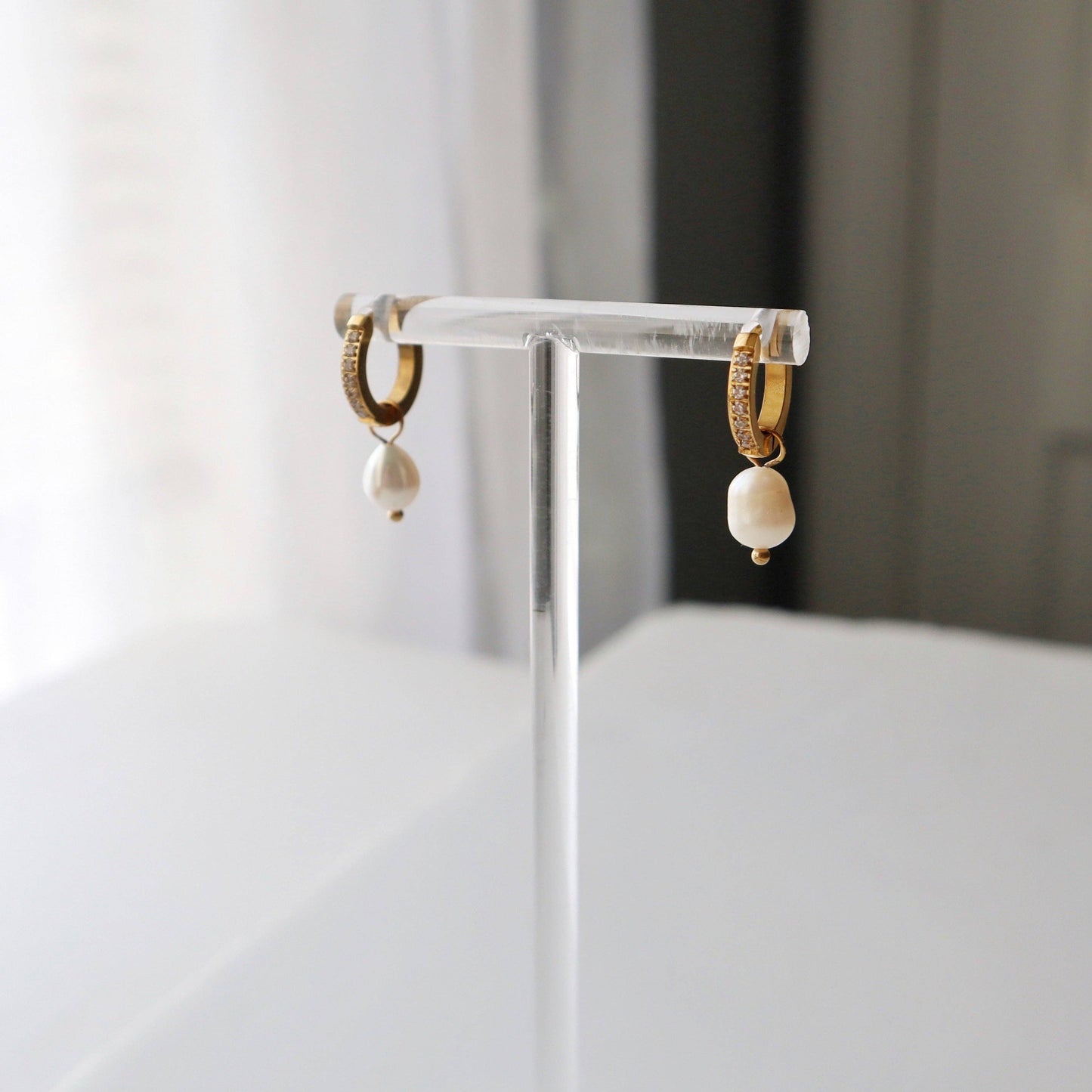 View of Gold CZ Huggies with Pearl Drop showcasing details from a clear acrylic jewelry stand. 